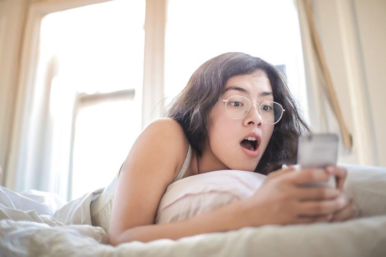 La_Risposta_di_Tamar_e_la_Reazione_del_Pubblico_xtQ5ntrqDb - Confidenze24 Source: Andrea Piacquadio - pexels - Young woman lying on bed, surprised by something on her smartphone, in a bright bedroom setting.