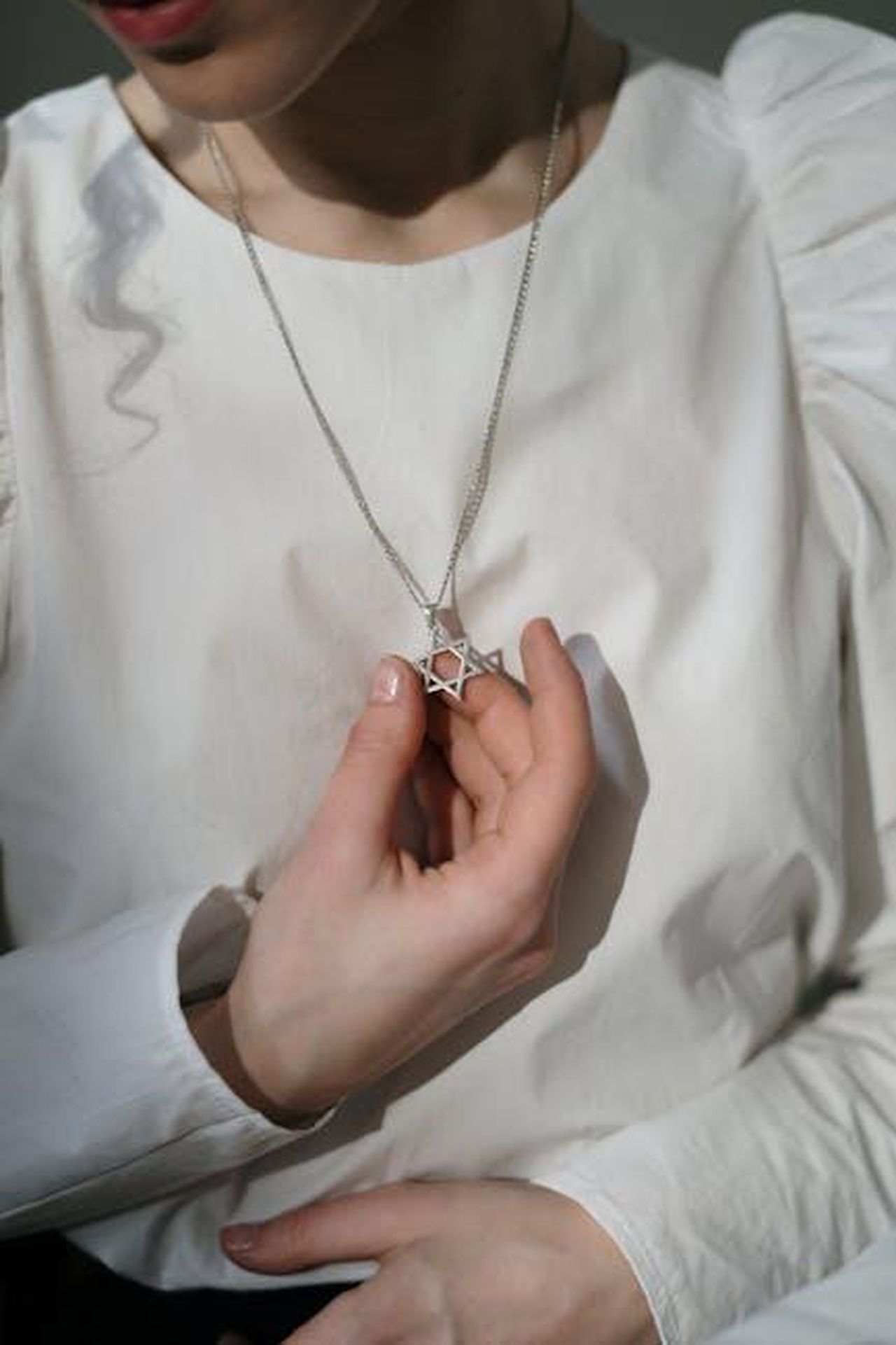 La_Speranza_di_Elton_di_Recuperare_la_Vista_HT79Y8yY0K - Confidenze24 Source: cottonbro studio - pexels - Close-up of a woman's hand holding a Star of David necklace on a white blouse.
