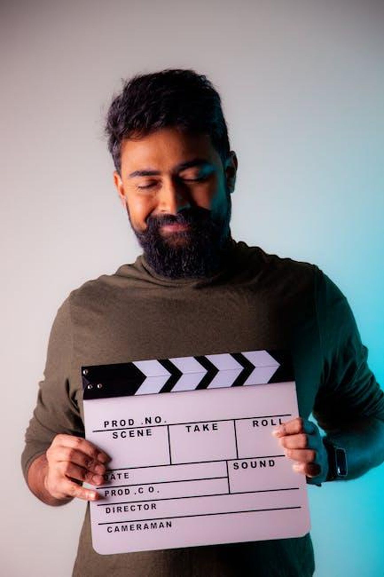 La_carriera_di_Isaiah_Stokes_JnSrXxiNki - Confidenze24 Source: Teja J - pexels - Portrait of a bearded man holding a clapperboard with eyes closed, smiling in a studio setting.