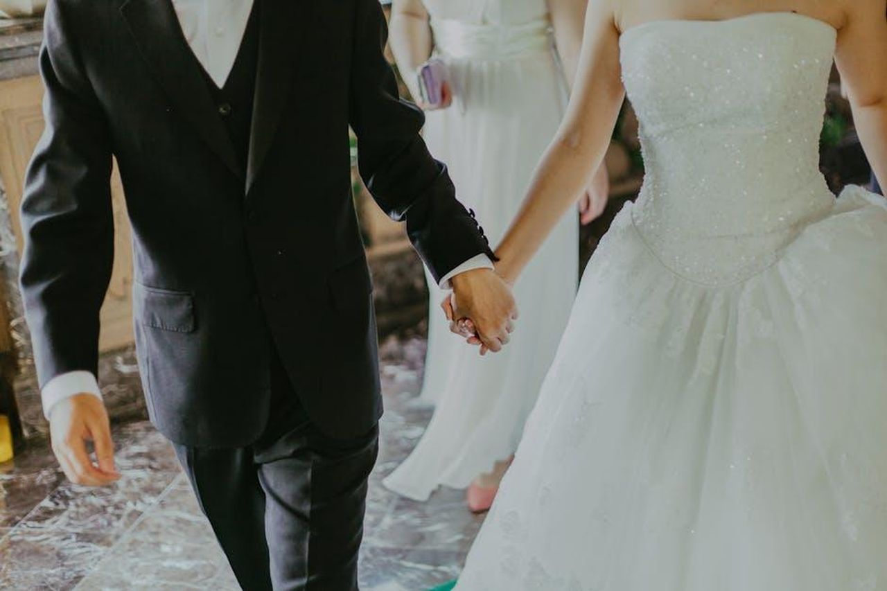 La_chiave_del_loro_matrimonio_rispetto_e_determinazione_OTSSrU7p3D - Confidenze24 Source: Jeremy Wong - pexels - A romantic moment capturing a bride and groom holding hands in elegant wedding attire indoors.