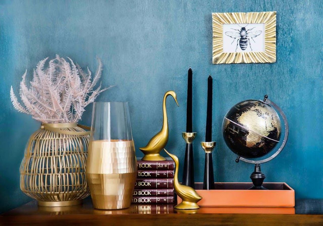 La_collaborazione_tra_LoveShackFancy_e_Pottery_Barn_qpSs2txYfT - Confidenze24 Source: Sammsara Luxury Modern Home - pexels - Stylish home decor arrangement including a globe, books, candles, and vases on a blue backdrop.
