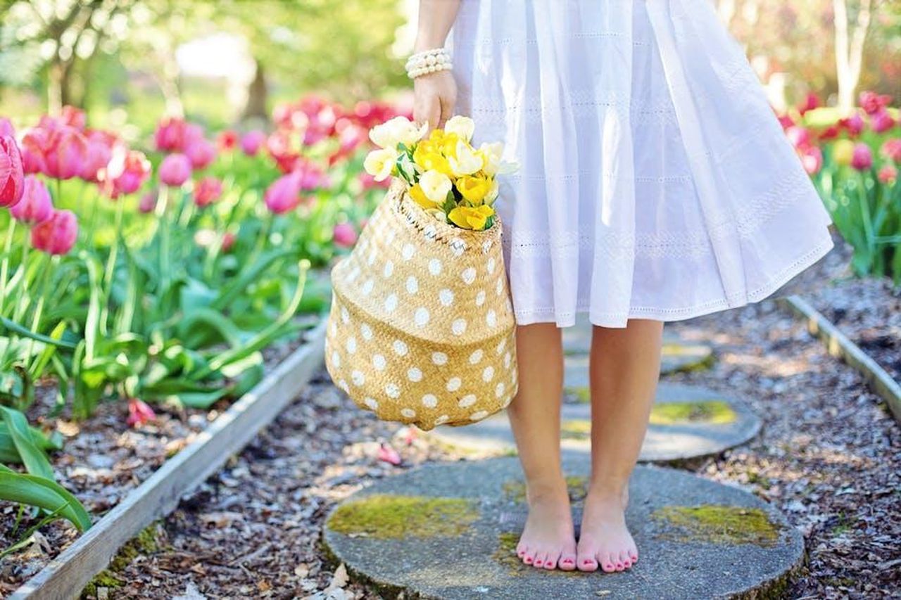 La_collezione_curata_da_Meghan_Markle_KkDjtHBFUC - Confidenze24 Source: Jill Wellington - pexels - A woman in a white dress carries a basket of yellow flowers while walking barefoot in a tulip garden.