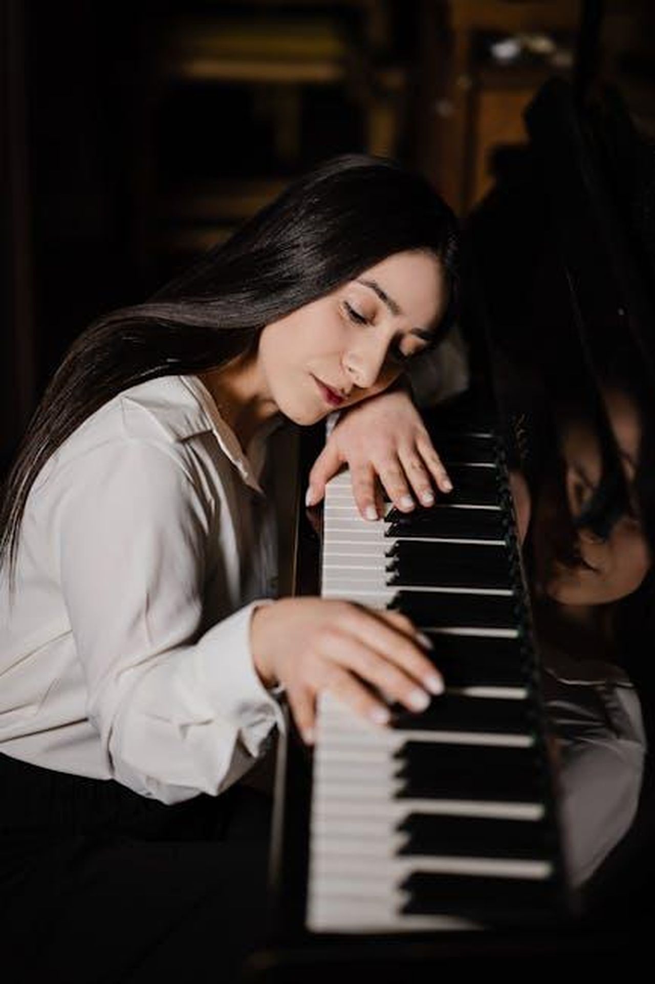 La_conferma_della_relazione_nella_nuova_canzone_di_Grande_rlFQCAGLHm - Confidenze24 Source: Павел Адамян - pexels - A peaceful woman rests on a grand piano, reflecting tranquility and connection to music.
