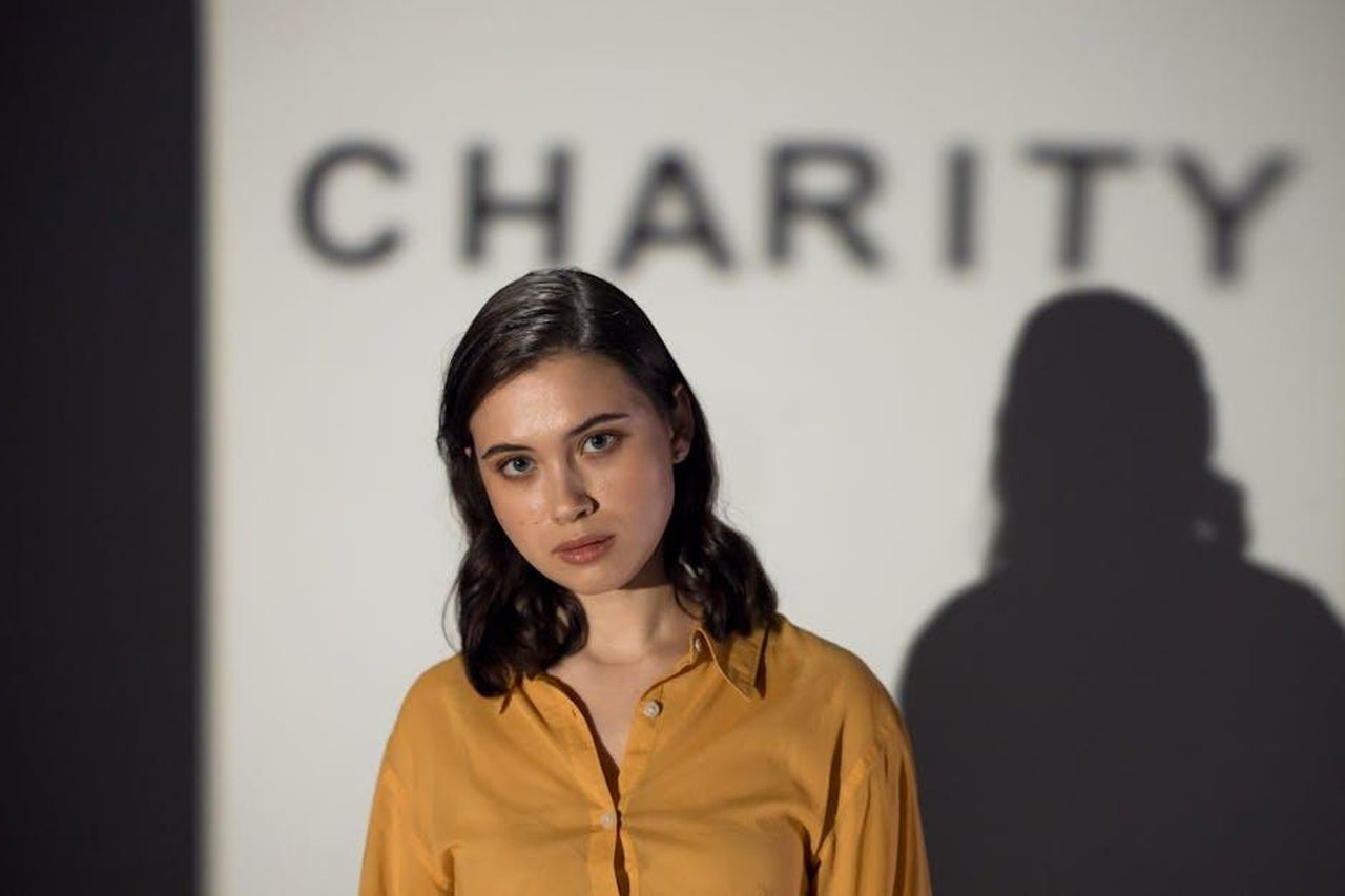 Source: Ron Lach - pexels - A thoughtful woman stands before a charity-themed backdrop, evoking compassion and volunteerism.