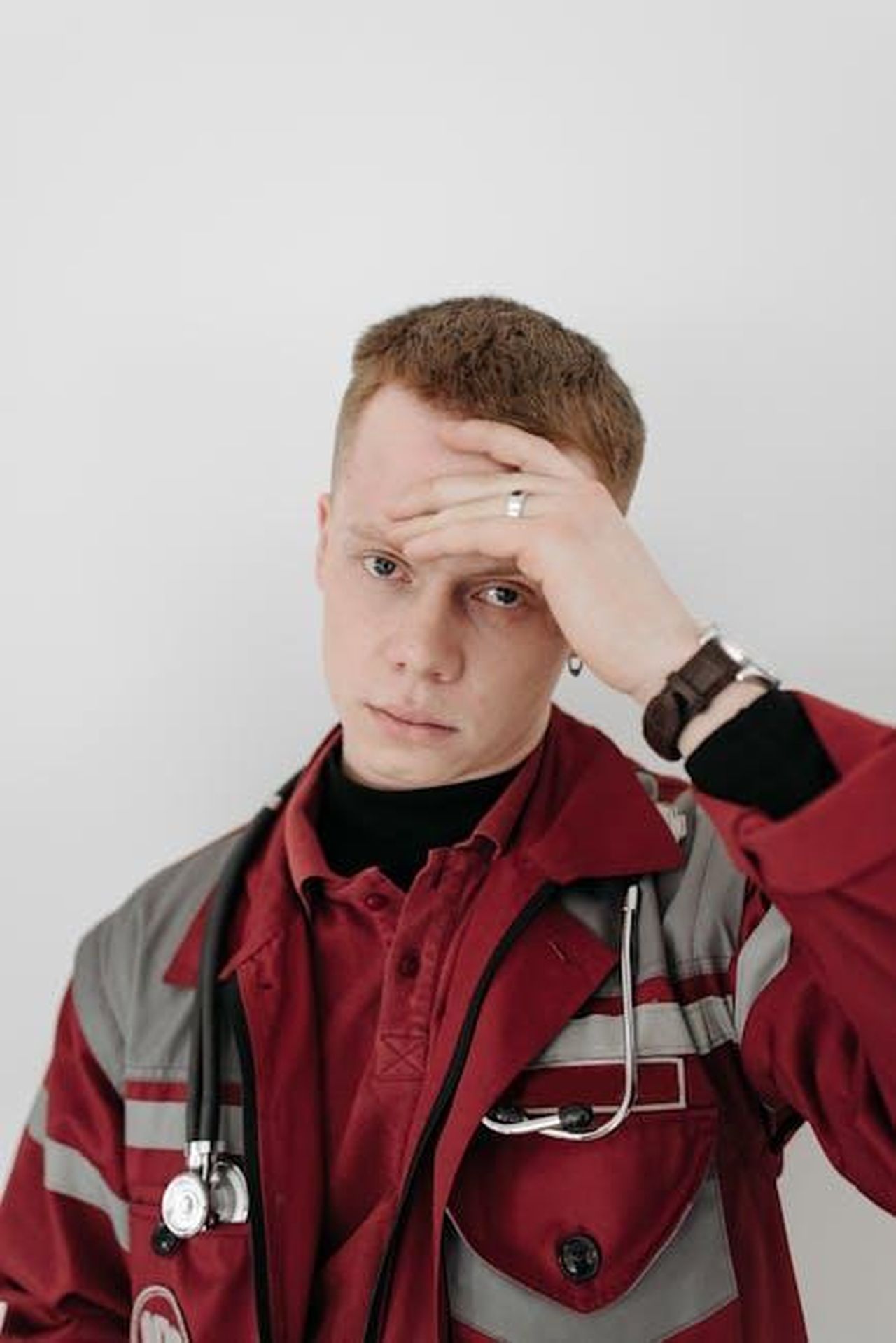 La_crisi_medica_del_loro_bambino_lhHbqN9DDp - Confidenze24 Source: Pavel Danilyuk - pexels - A tired EMT in uniform holds his head, exhibiting stress in a healthcare setting.