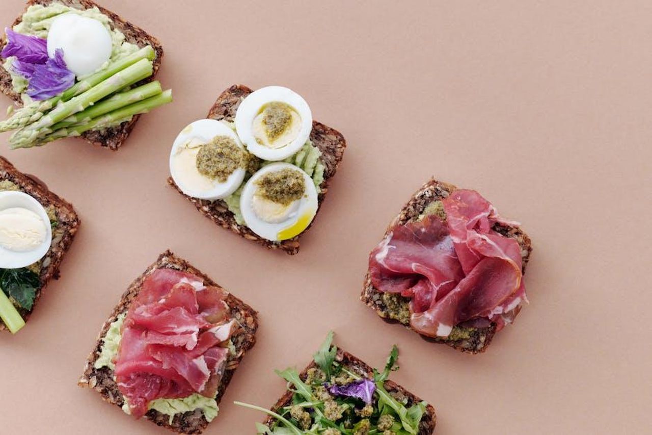 La_critica_di_Michael_Symon_alla_ricetta_virale_delle_uova_al_pesto_gkRHhSB1Fn - Confidenze24 Source: Luna Lovegood - pexels - Delicious open-faced sandwiches with gourmet toppings including eggs, ham, and asparagus on rustic bread.
