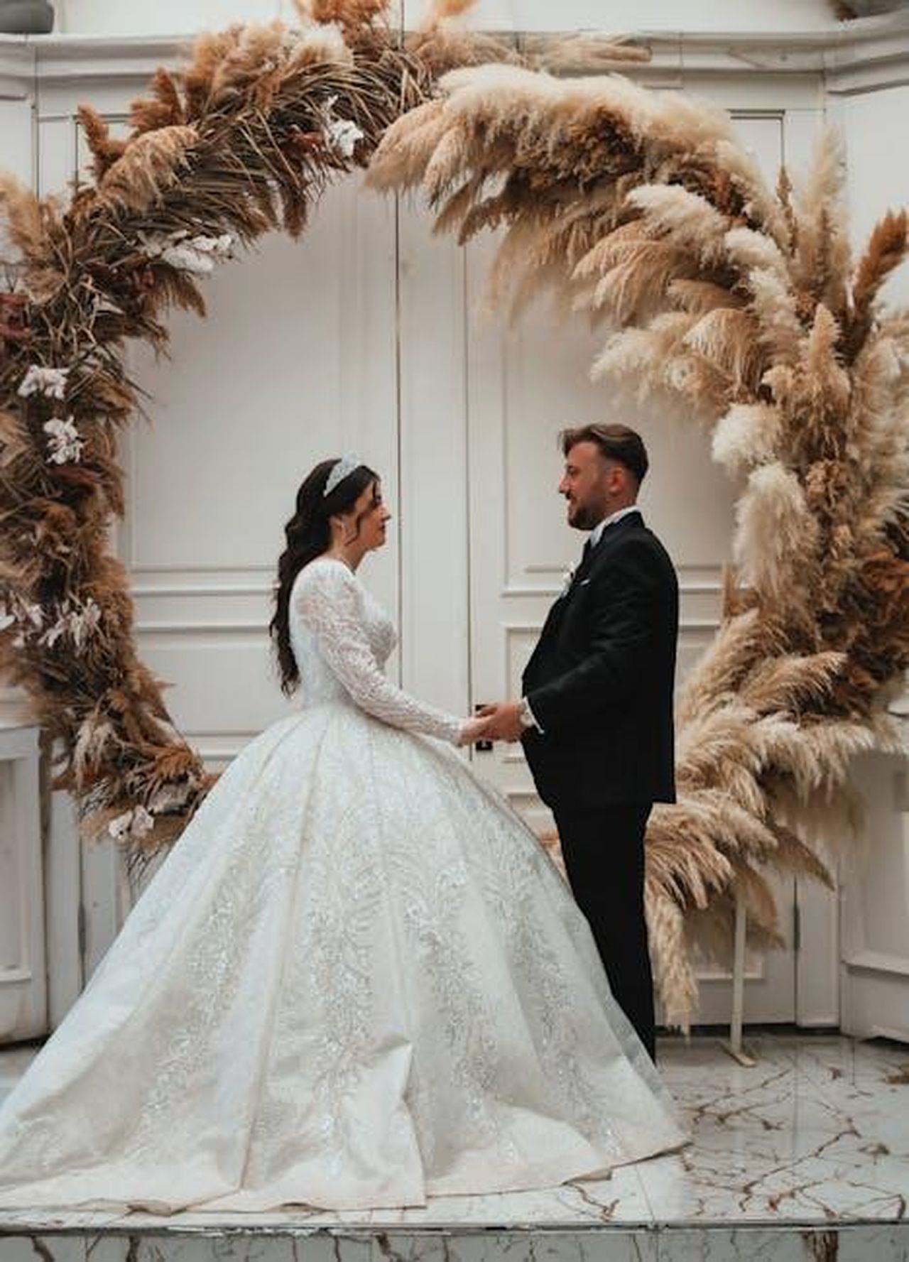 La_difesa_della_moglie_di_Goldblum_lOi3UQ8su6 - Confidenze24 Source: Olcay Ertem - pexels - A couple in elegant attire stands under a pampas grass arch during their indoor wedding in Ankara, Türkiye.
