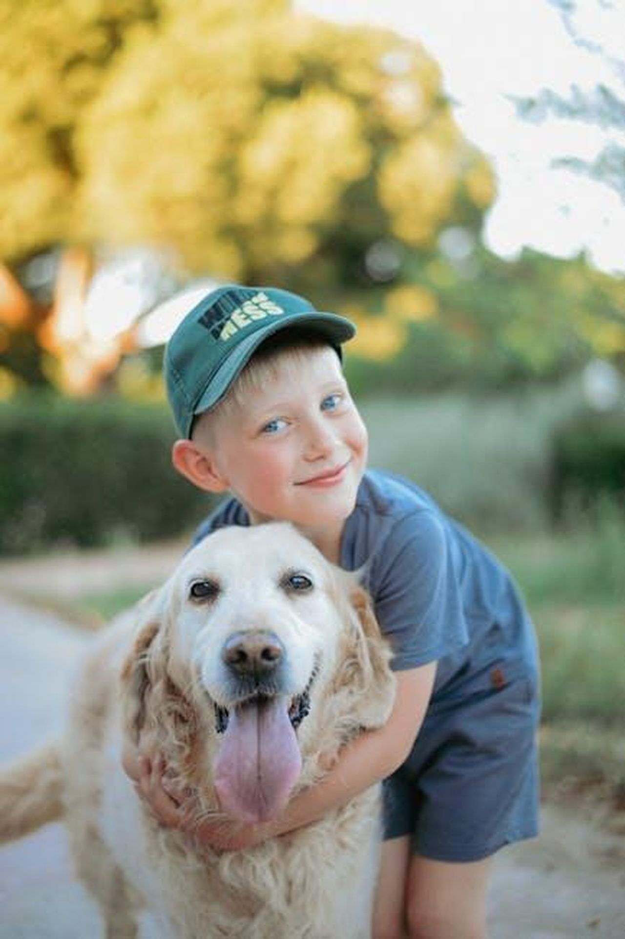 La_dolcezza_di_Grace_e_Stella_SsKbDfpBz5 - Confidenze24 Source: Daka - pexels - A joyful child in a blue outfit hugs a happy golden retriever outside on a sunny day.