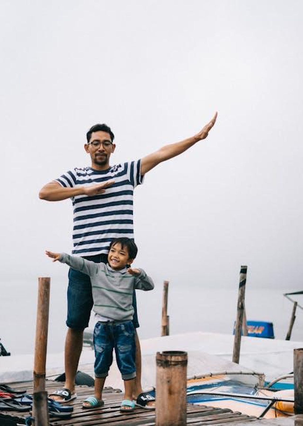 La_famiglia_di_Katherine_e_Chris_un_quadro_completo_43WAhuiXk4 - Confidenze24 Source: Agung Pandit Wiguna - pexels - Father and son posing playfully on a wooden dock by the water, enjoying a day outdoors.