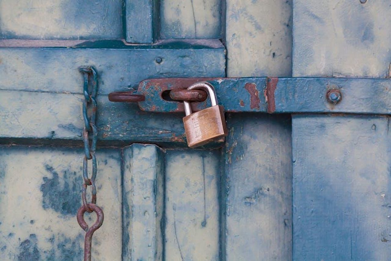 La_filosofia_di_vita_della_famiglia_Olsen_UKruab5fok - Confidenze24 Source: Pixabay - pexels - A close-up of a rusty padlock securing a blue painted wooden door with chain and bolt.