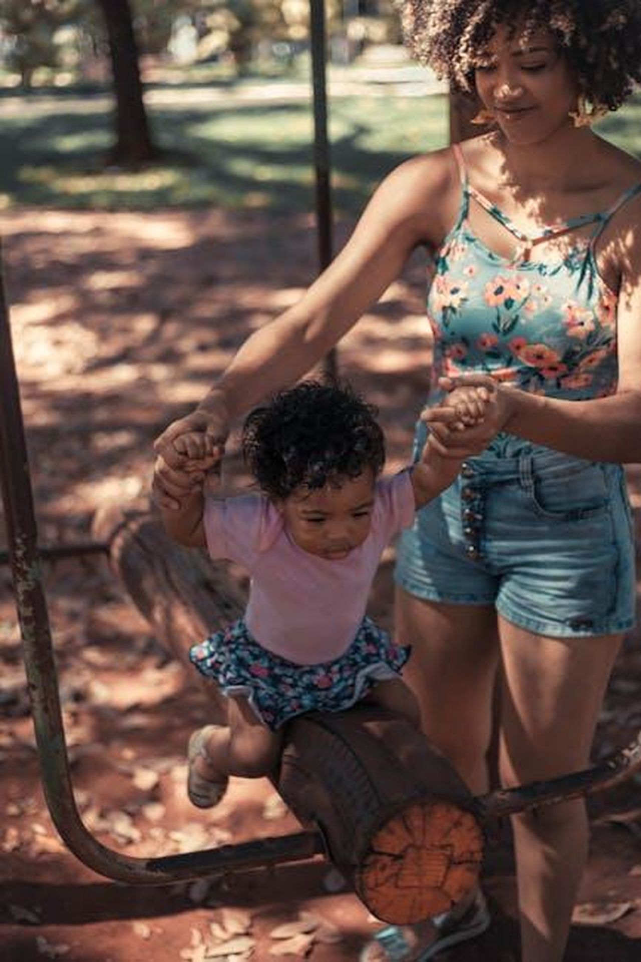 La_gioia_della_maternit_per_Brittany_VEmyNlmdUy - Confidenze24 Source: Orione Conceição - pexels - A joyful moment of a mother assisting her daughter on a log in a sunny park, depicting family bonding and fun.