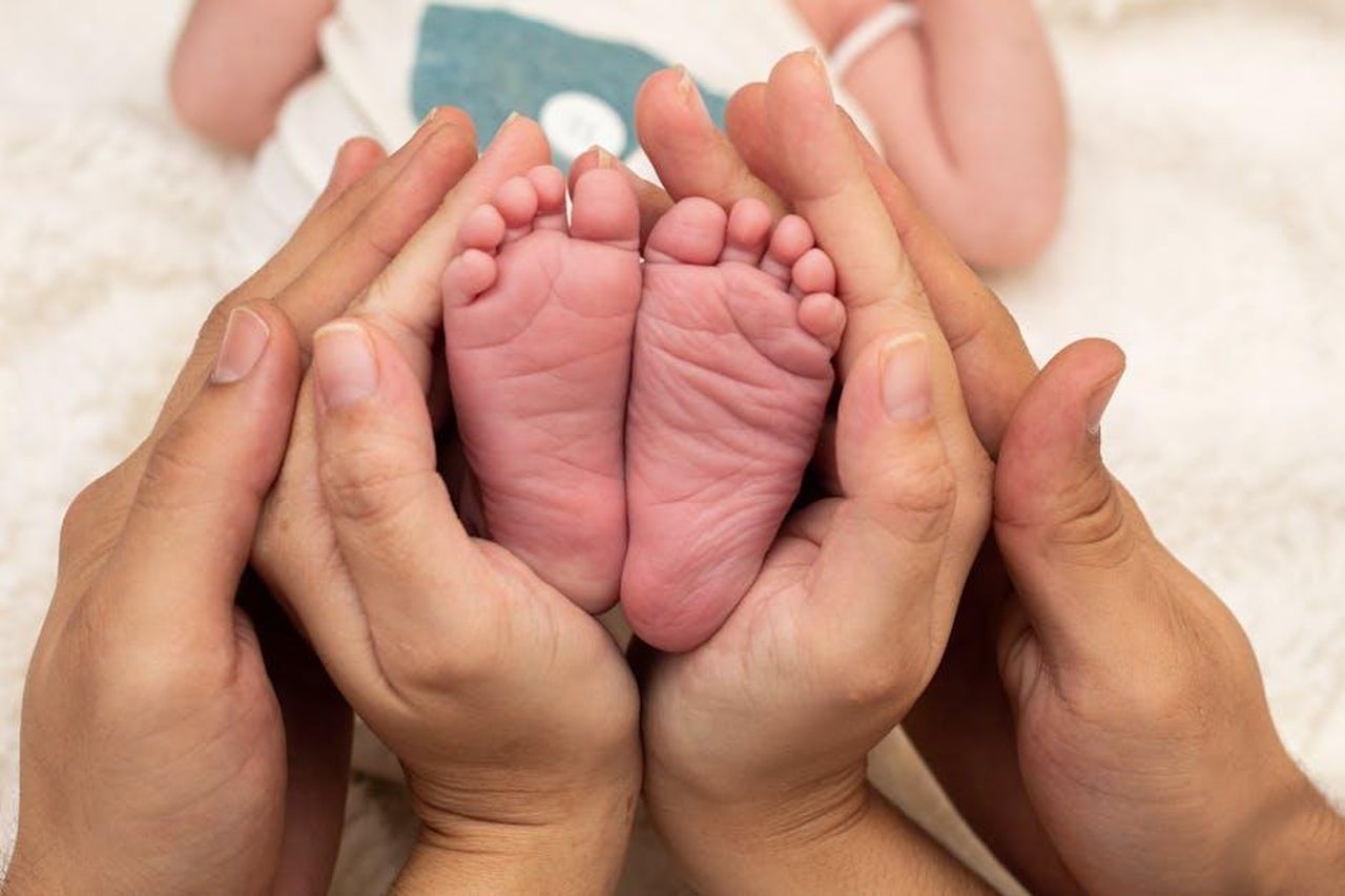 La_loro_famiglia_allargata_LfMu8uljHw - Confidenze24 Source: A Retratista - pexels - Close-up of a baby's feet cradled tenderly by parents' hands, symbolizing love and care.