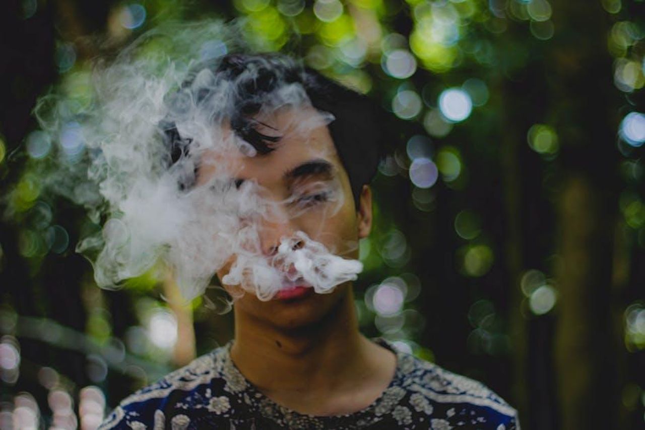La_lotta_contro_le_dipendenze_z9bv0GmMfw - Confidenze24 Source: Joey Theswampboi - pexels - A young man smoking and exhaling smoke outdoors with a blurred natural background.