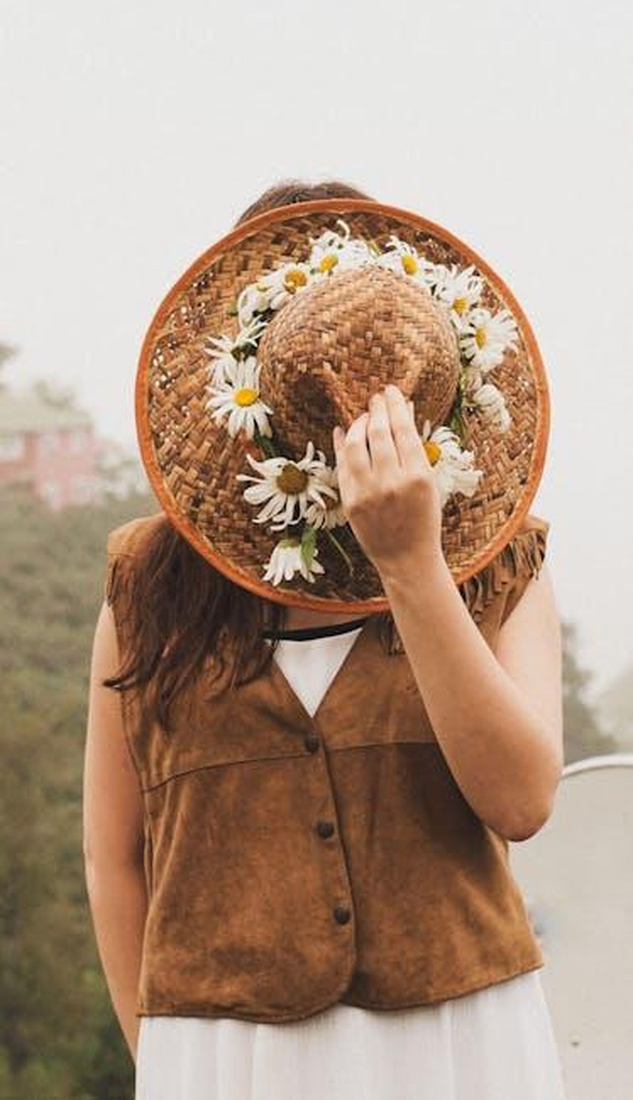 La_passione_di_Meghan_per_larrangiamento_dei_fiori_TD0UMIGBZU - Confidenze24 Source: Duygu - pexels - Woman wearing brown vest and straw hat adorned with daisies stands outdoors, face obscured.