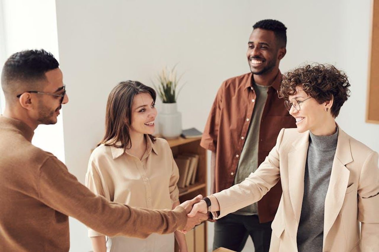 La_passione_per_gli_affari_di_Barron_Trump_wQ6e6dEsgq - Confidenze24 Source: fauxels - pexels - Four colleagues smiling and shaking hands in a bright office setting.