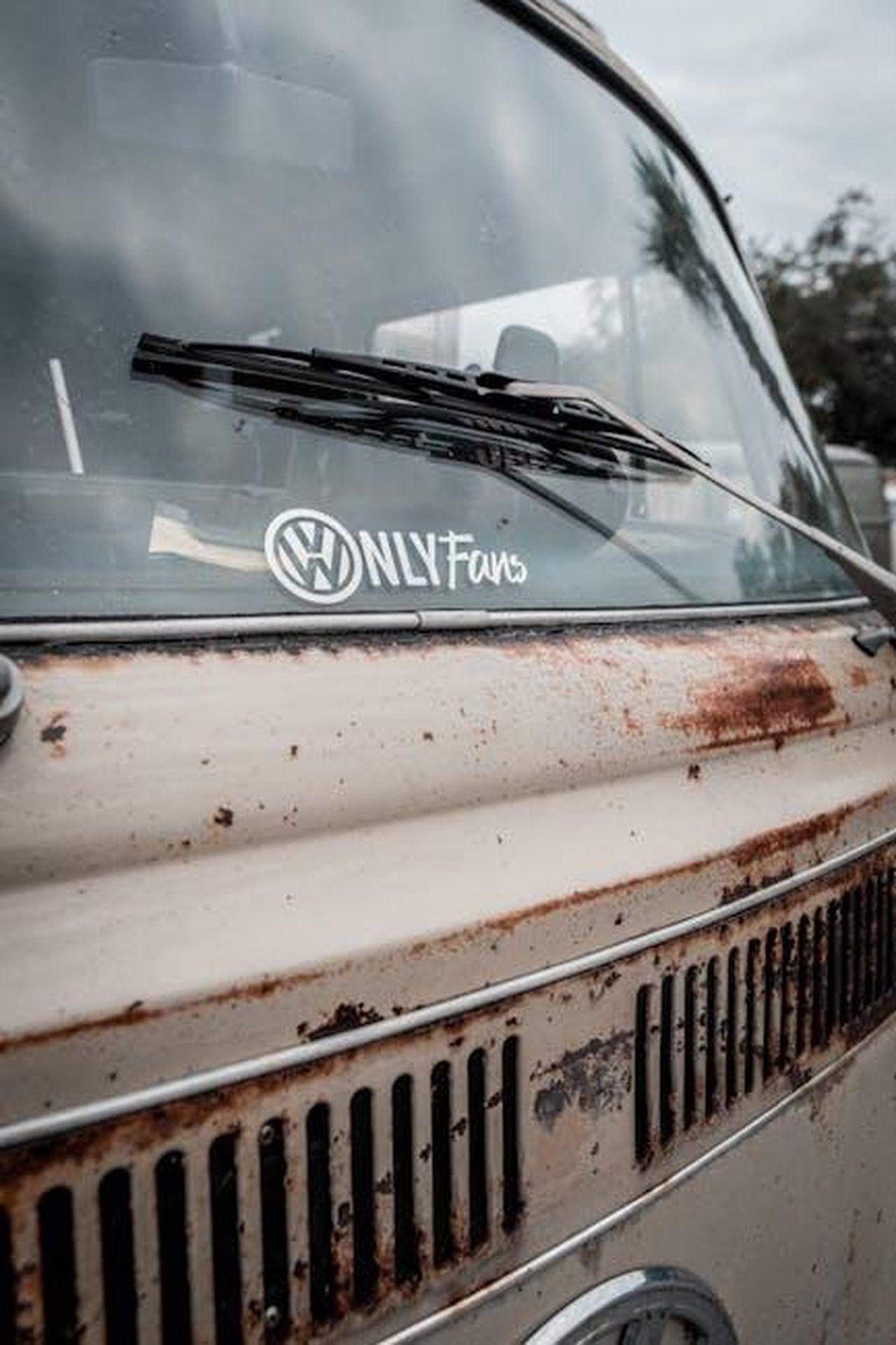 La_posizione_di_Denise_Richards_su_OnlyFans_hIlVQdiSNu - Confidenze24 Source: Connor McManus - pexels - Close-up of a rusty Volkswagen van's windshield featuring a humorous sticker and wiper.