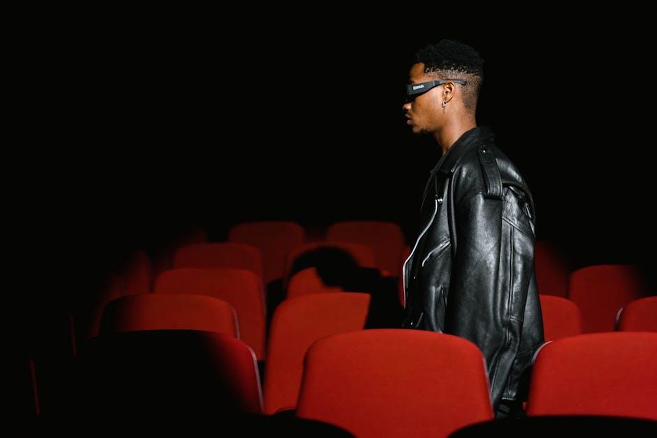 La_premiere_di_The_Accountant_2_al_SXSW_160k6ikBYx - Confidenze24 Source: Tima Miroshnichenko - pexels - A man wearing glasses walks through a dimly lit movie theater with red seats.