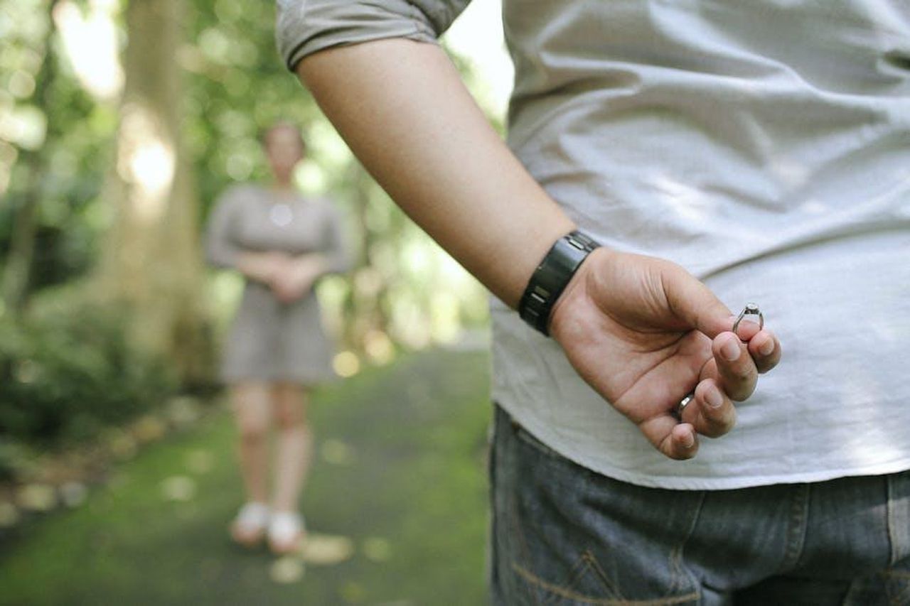 La_proposta_di_matrimonio_di_Reedus_Nrs1ElfdyC - Confidenze24 Source: Daniel Moises Magulado - pexels - A man hides an engagement ring behind his back, preparing to propose in a picturesque park setting.