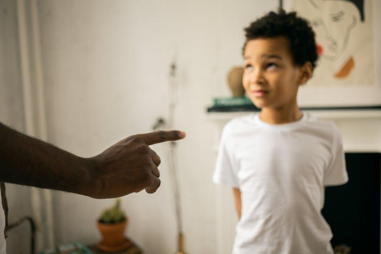 La_reazione_dei_fan_e_della_famiglia_mtc0FeyrUC - Confidenze24 Source: Monstera Production - pexels - A father points and scolds his son indoors, emphasizing discipline.