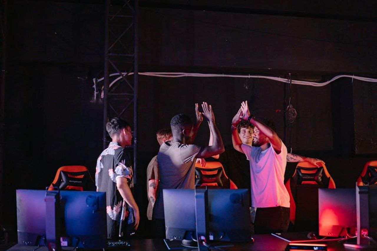 La_reazione_della_comunit_e_le_implicazioni_YbNAZXyQ5t - Confidenze24 Source: Yan Krukau - pexels - A diverse group of young gamers celebrating a victory with high-fives in a dark gaming room.