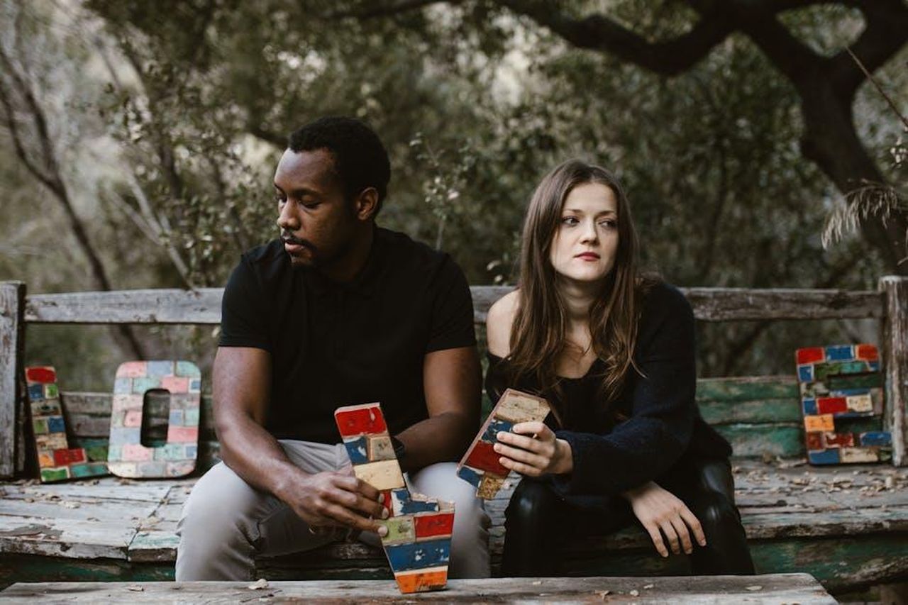 La_reazione_di_Ben_alla_rottura_con_Sara_xiTycnIthA - Confidenze24 Source: RDNE Stock project - pexels - A couple sits in tension on a bench surrounded by nature, holding colorful blocks spelling 'Love'.