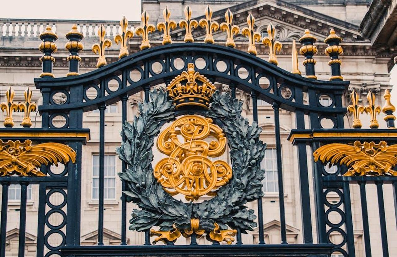 La_reazione_di_Buckingham_Palace_2NfbwFqXAc - Confidenze24 Source: Roméo - pexels - Detailed view of the ornate gold and black iron gate at Buckingham Palace, London.