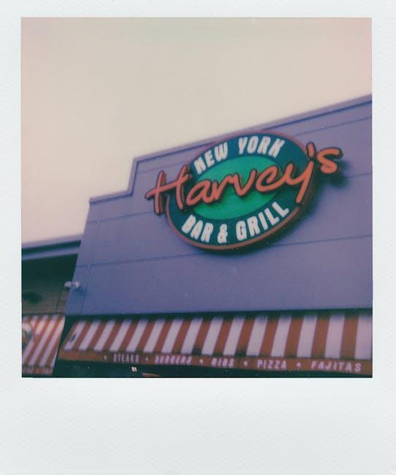 La_reazione_di_Harvey_Weinstein_al_discorso_di_Brody_ipDyO0HdqS - Confidenze24 Source: Lisa from Pexels - pexels - Vintage-style polaroid showing Harvey's Bar and Grill storefront with retro signage.