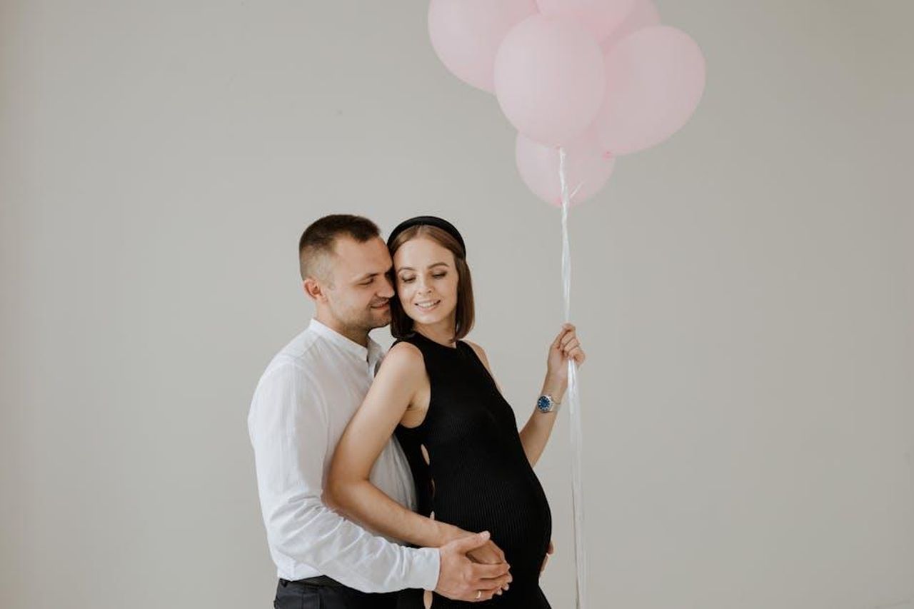 La_reazione_di_Vivian_alla_transizione_e_alle_aspettative_di_genere_ZluRAgXxzQ - Confidenze24 Source: RDNE Stock project - pexels - A loving couple celebrating maternity with pink balloons in a studio setting.