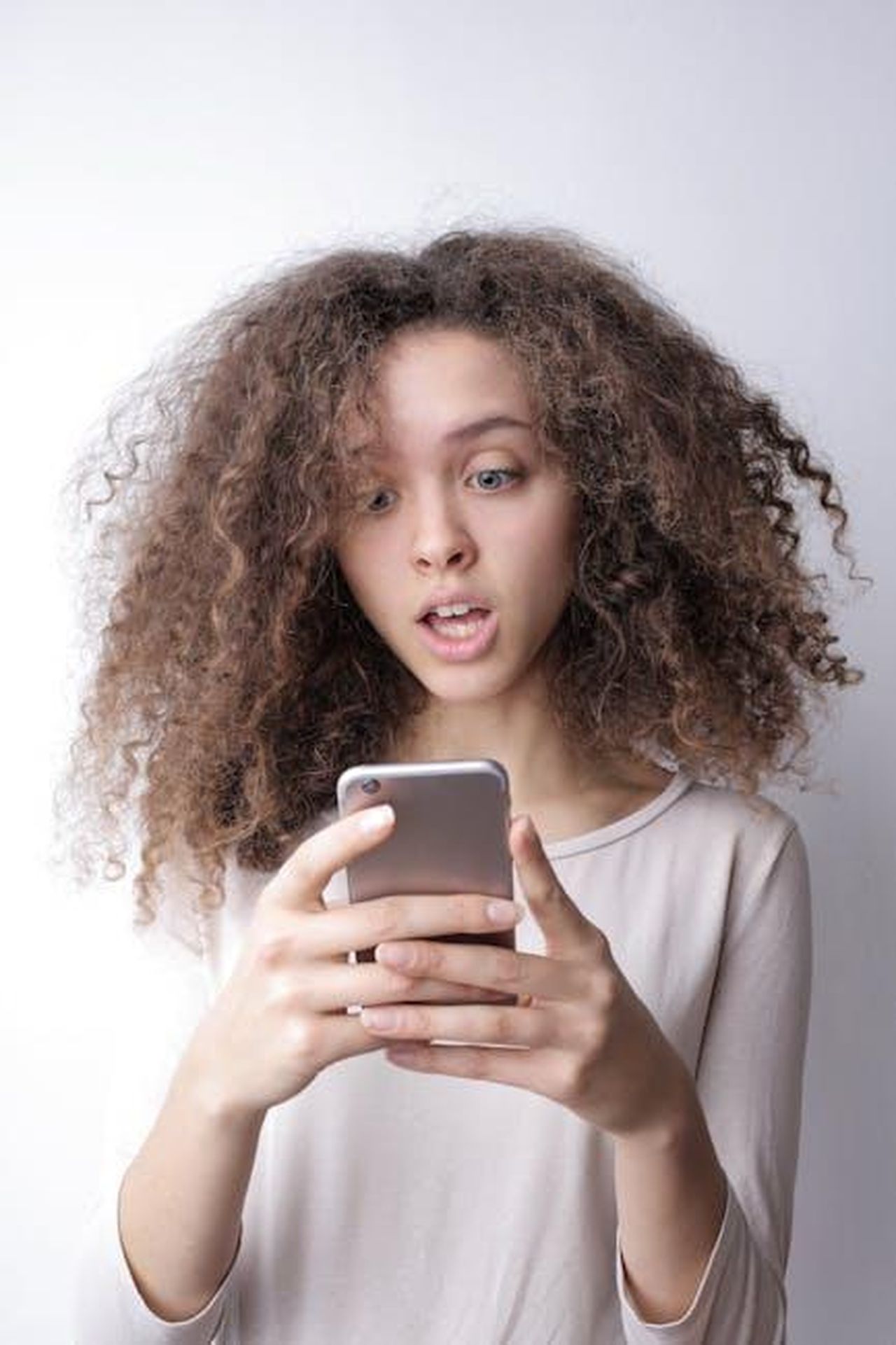 La_reazione_sui_social_e_la_rettifica_di_Smith_oCKXjOFnUd - Confidenze24 Source: Andrea Piacquadio - pexels - A young woman with curly hair looks surprised while reading something on her smartphone indoors.