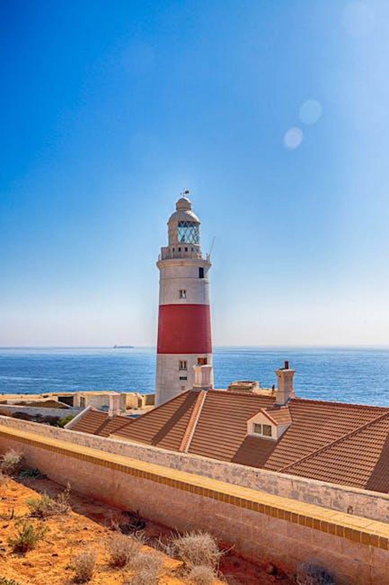 La_rebellious_greatgrandmother_1Q7c9fwqqo - Confidenze24 Source: Kent Kan - pexels - A picturesque lighthouse stands tall by the ocean, surrounded by a serene coastal landscape under a clear blue sky.