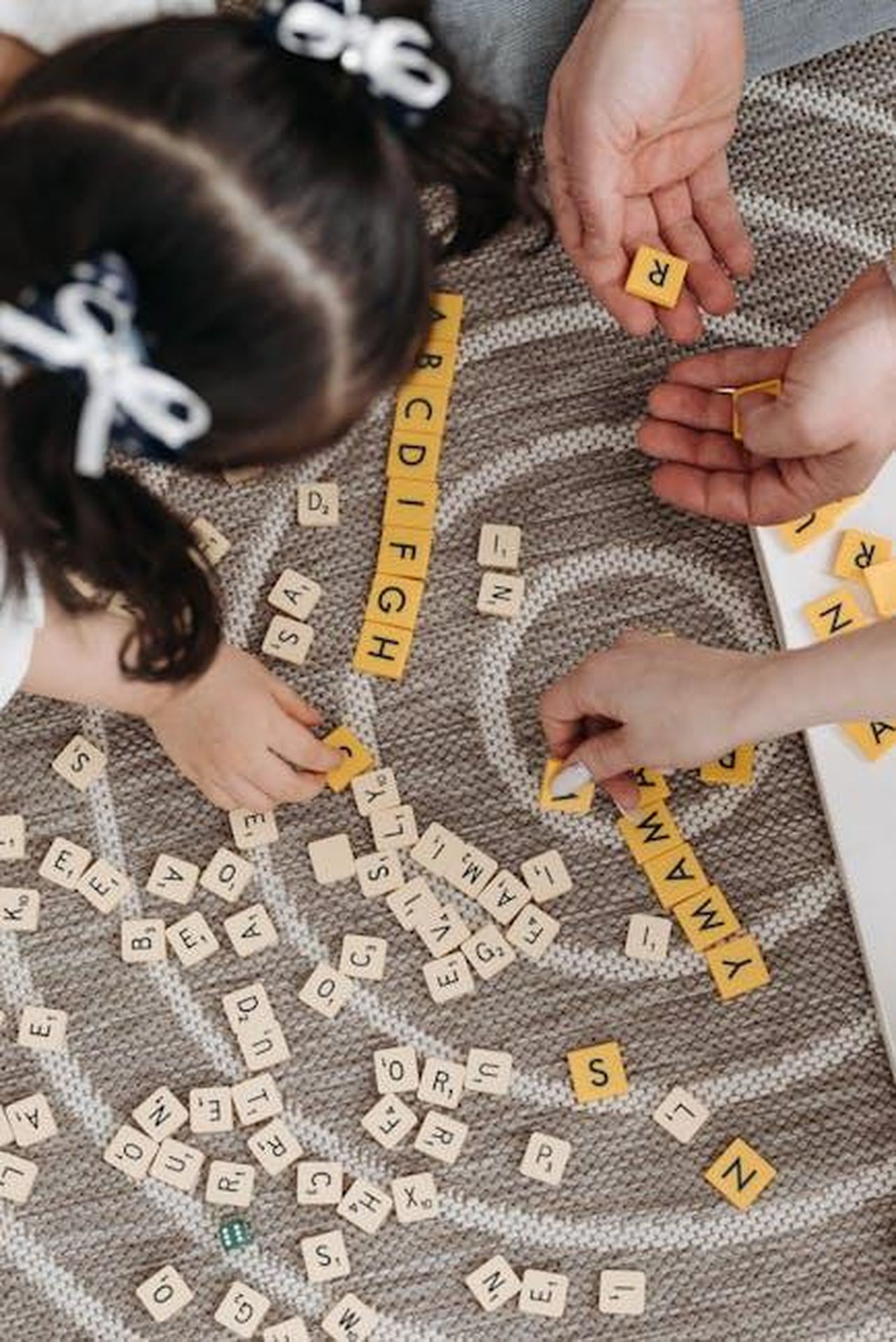 La_relazione_di_Justine_con_i_figli_di_Elon_RKL7dsdHQs - Confidenze24 Source: Pavel Danilyuk - pexels - Family playing a word game with tiles on a patterned carpet, showcasing togetherness and learning.