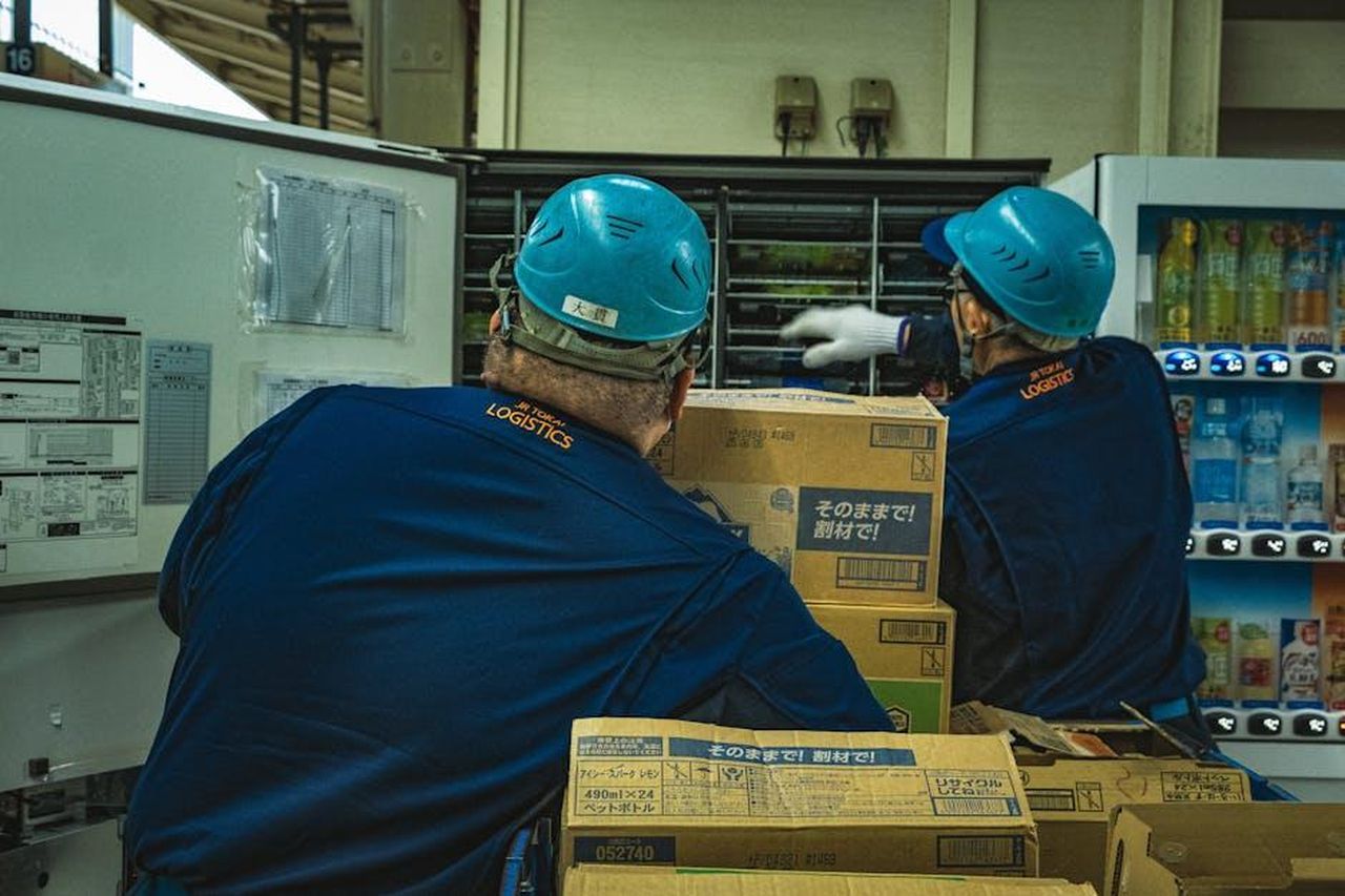 La_relazione_di_Meghan_con_il_team_di_produzione_Y5YGLPXcNJ - Confidenze24 Source: gabriele donofrio - pexels - Two workers in a warehouse managing logistics and organizing boxes near a vending machine.