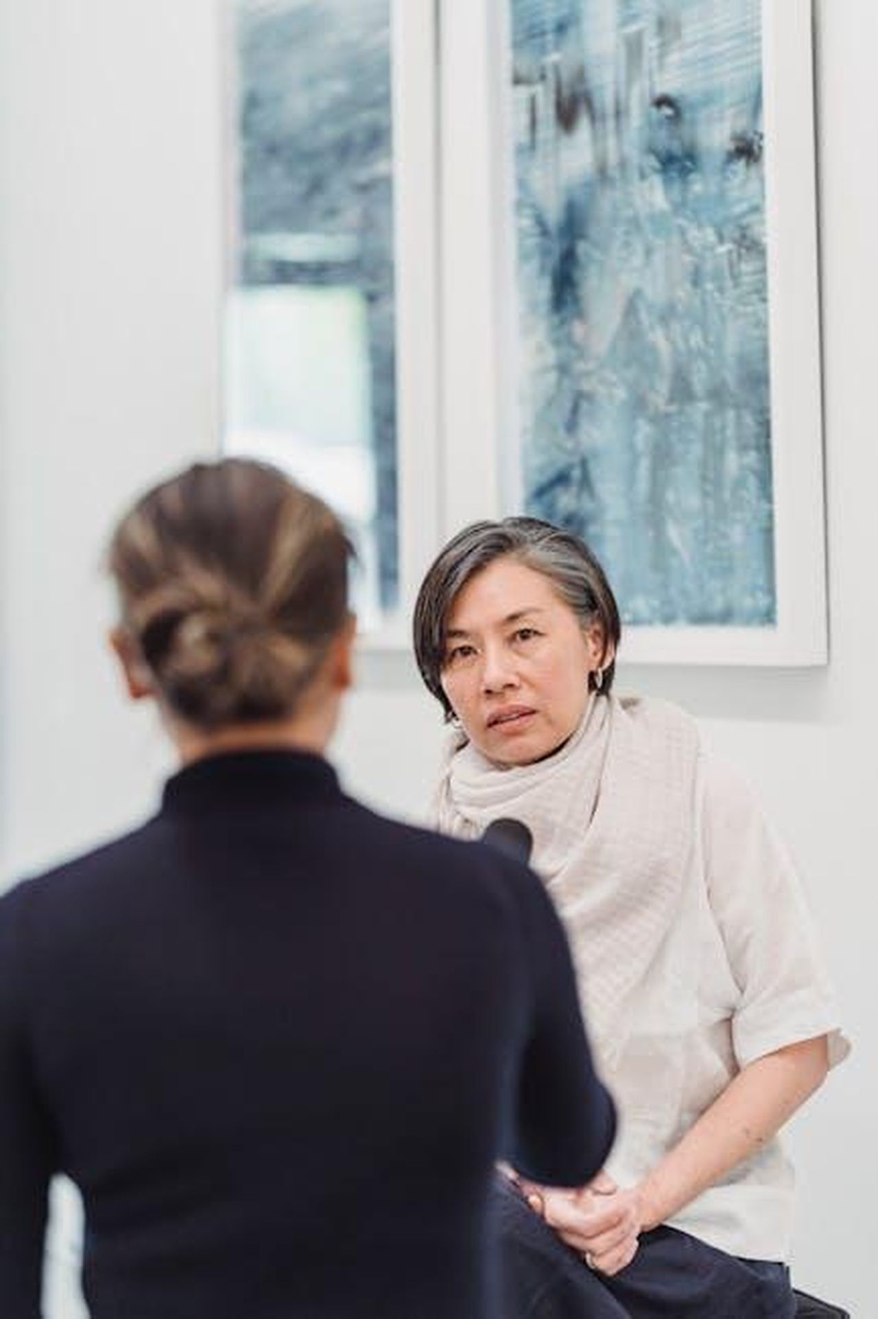 La_risposta_di_Us_Weekly_e_le_smentite_95dr8IhQFL - Confidenze24 Source: Greta Hoffman - pexels - Two women engaged in a professional interview indoors with artwork in the background.