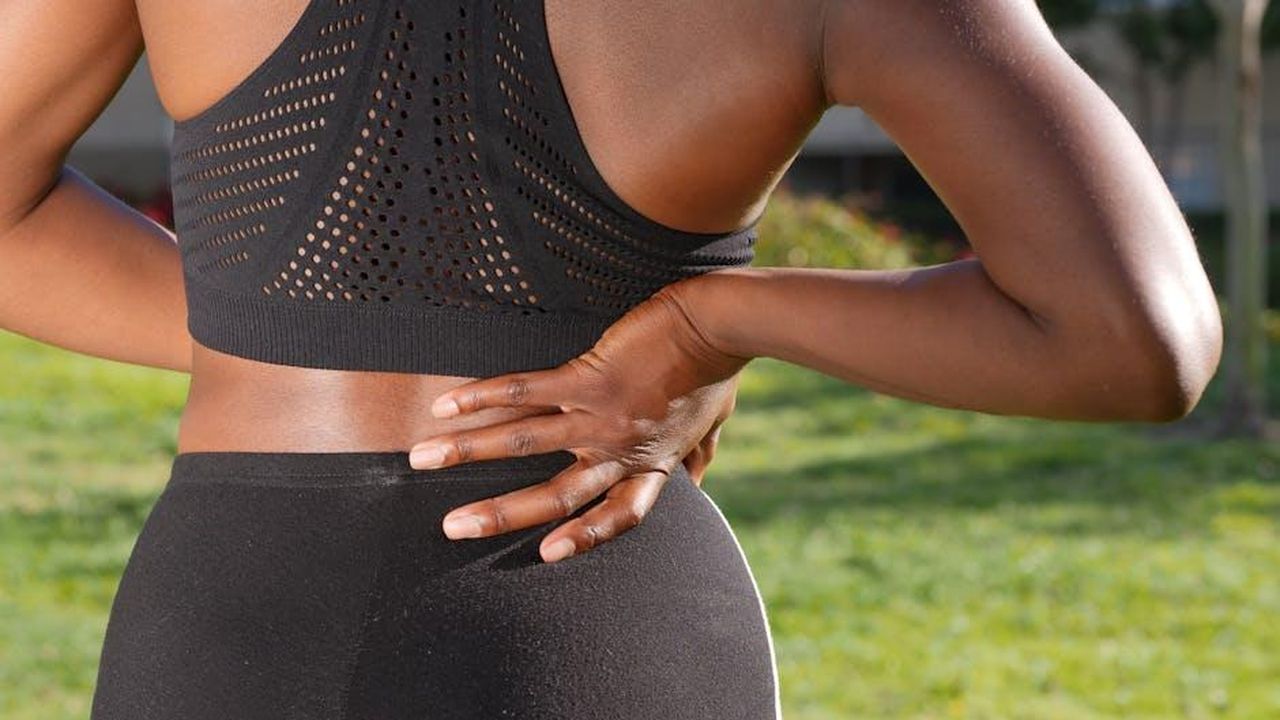 La_routine_di_fitness_di_Salma_Hayek_eg6hX9TF5y - Confidenze24 Source: Kindel Media - pexels - Woman in athletic attire holding her back outside, indicating discomfort or pain.