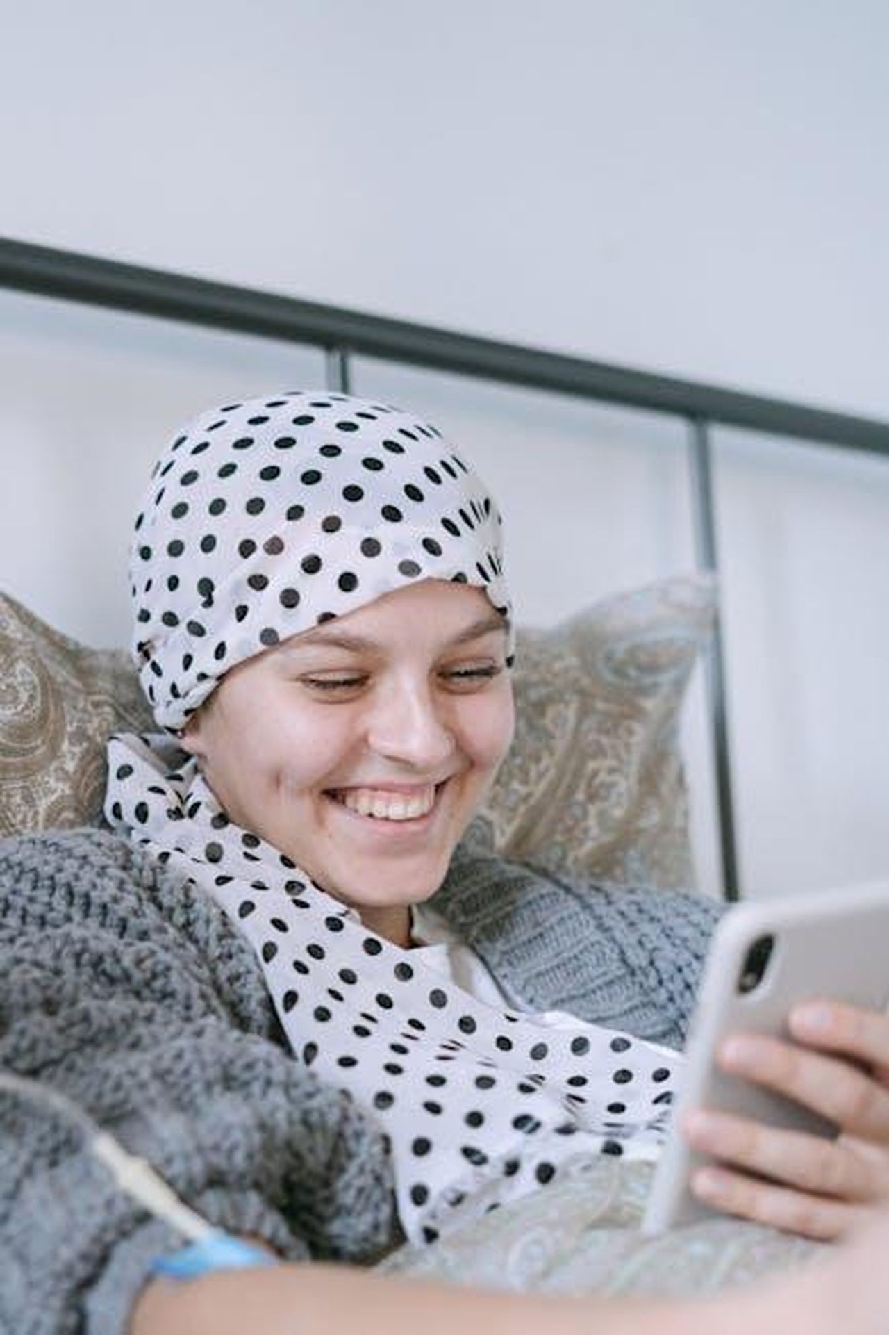 La_salute_del_Re_e_il_suo_trattamento_F7s4wc4R85 - Confidenze24 Source: Ivan Samkov - pexels - A woman with a polka dot scarf smiles while using her smartphone in bed.
