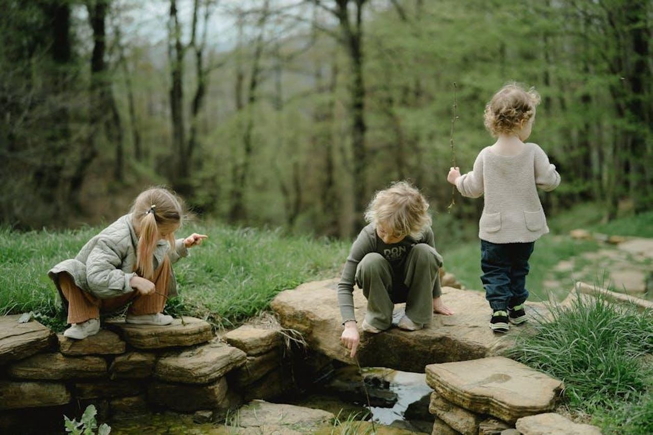 La_scoperta_di_Vivian_sui_suoi_fratelli_35vUtLtbUZ - Confidenze24 Source: Anastasia Shuraeva - pexels - Three children playing by a stone-lined stream in a lush green forest during springtime.