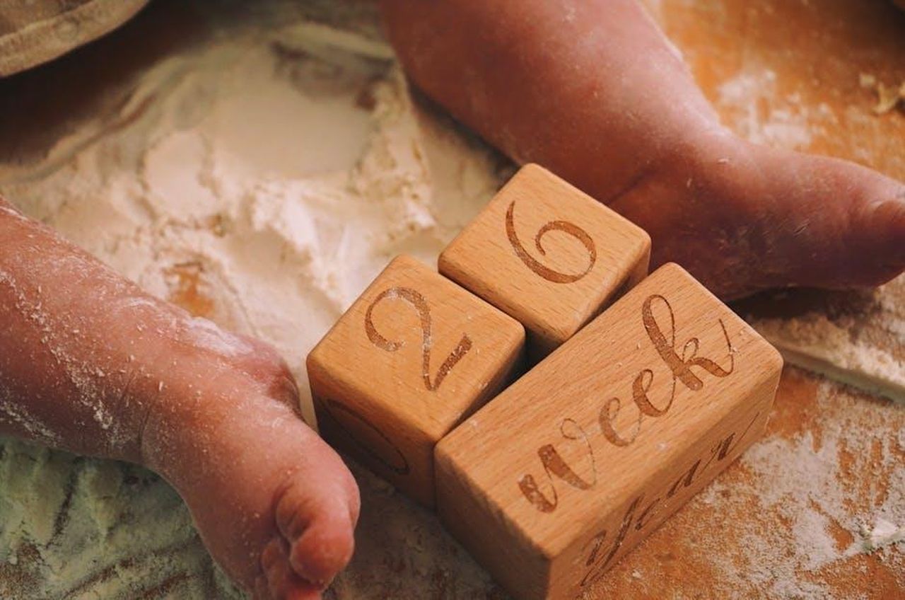 La_settimana_della_famiglia_nel_programma_XWjMXFMghZ - Confidenze24 Source: Griselda Belba - pexels - Adorable baby feet on flour-covered surface, next to wooden milestone blocks displaying 26 weeks.
