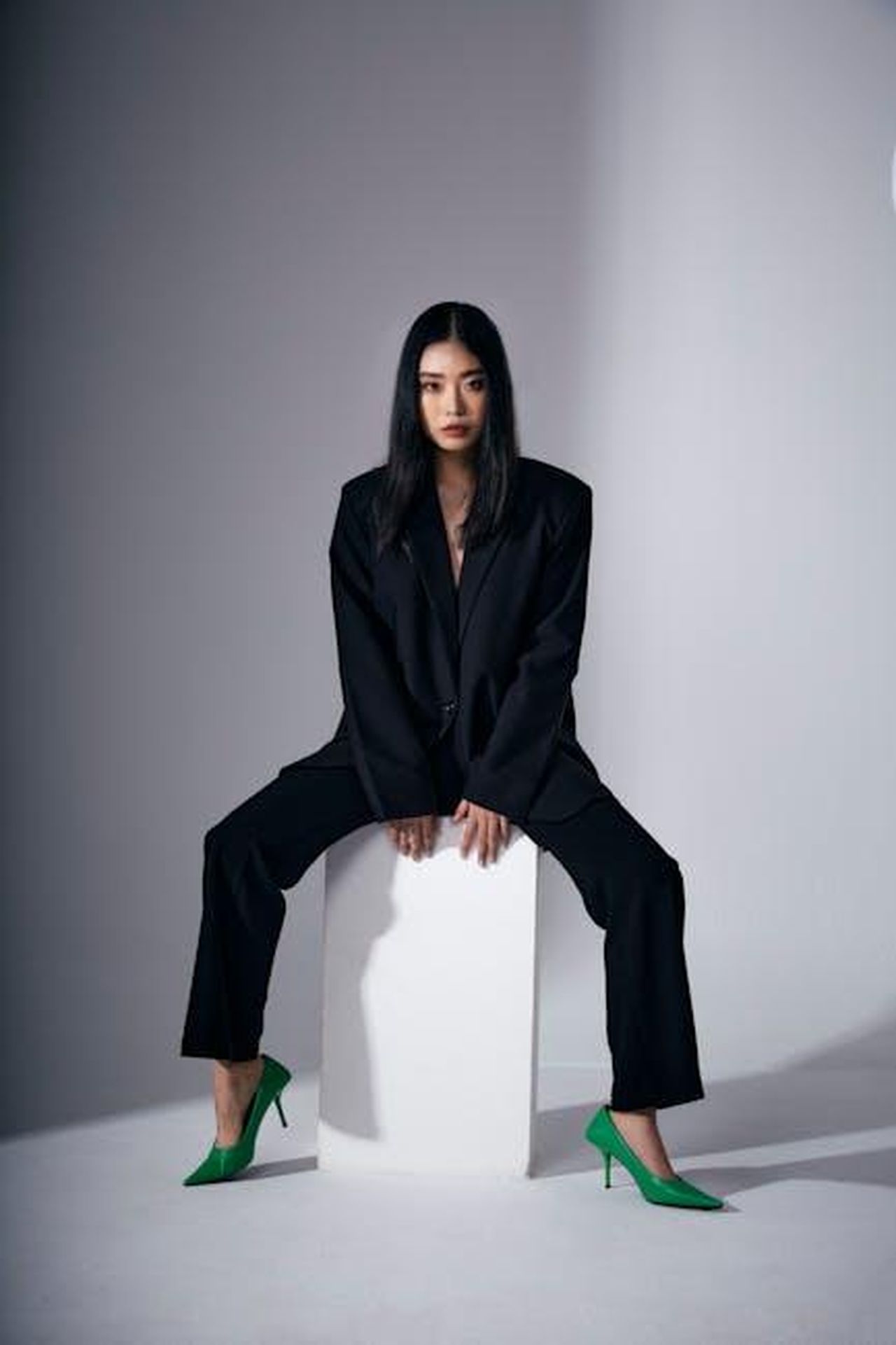 La_sicurezza_di_Ellen_Pompeo_nel_suo_stile_fJt53xS9uR - Confidenze24 Source: Hy Le - pexels - Striking fashion portrait featuring a woman in a black suit and green heels sitting on a block.