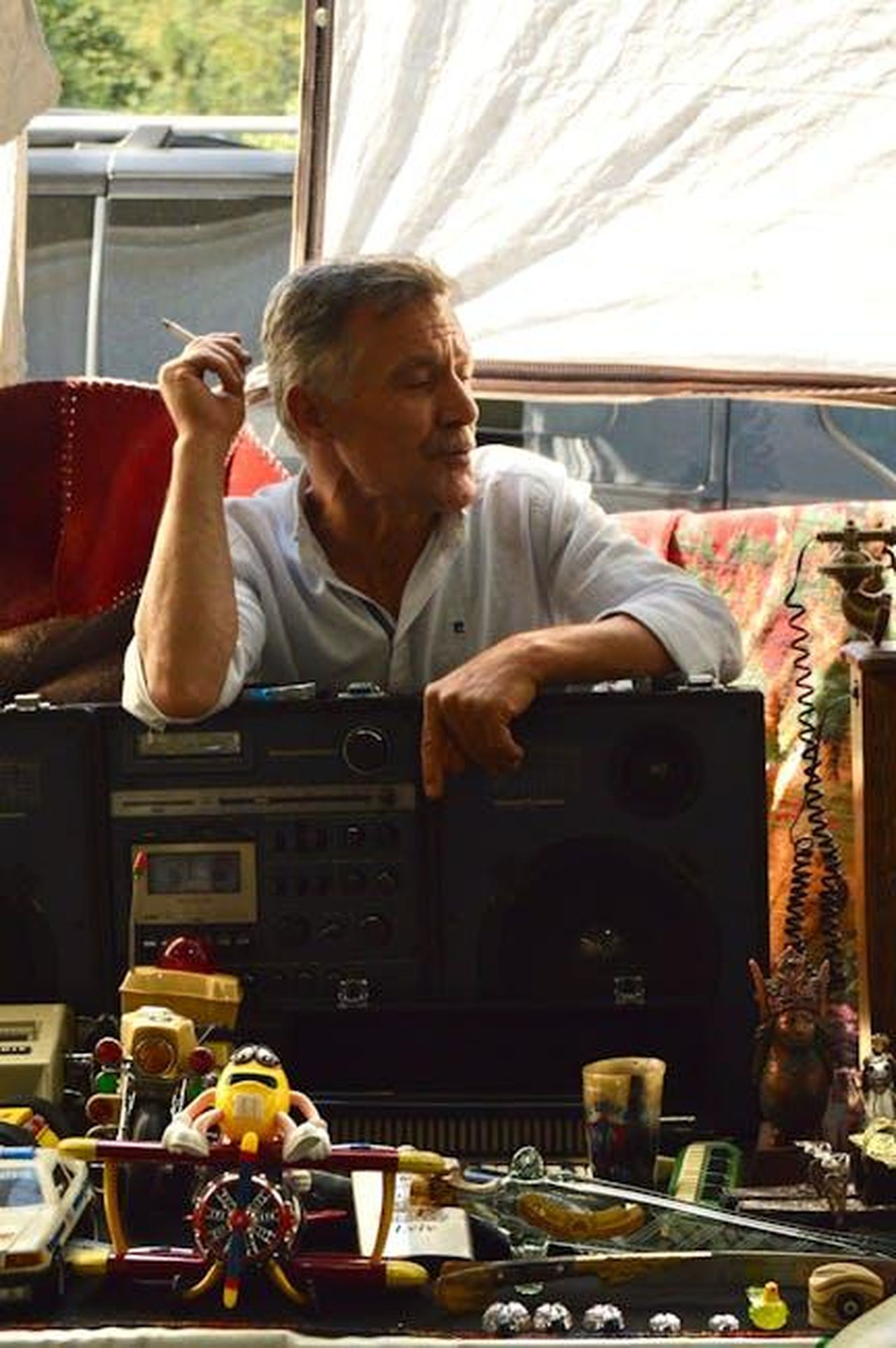 La_spiegazione_di_Ty_sulla_sua_assenza_d4JbULhUPj - Confidenze24 Source: Ayşenur - pexels - A relaxed man smokes while leaning on a vintage radio amidst eclectic decorations.
