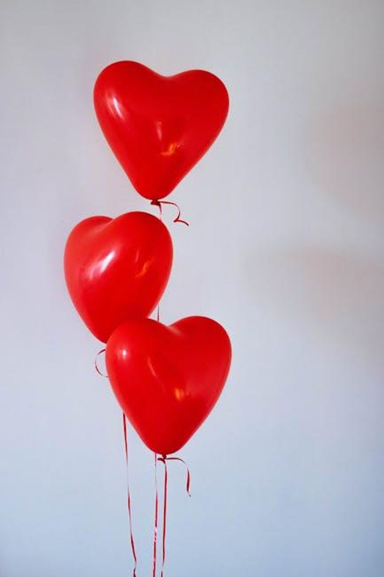 La_storia_damore_tra_Dolly_e_Carl_s7wnUsHy6N - Confidenze24 Source: Kristina Paukshtite - pexels - Three red heart-shaped balloons floating in a minimalist studio setting, evoking love and romance.
