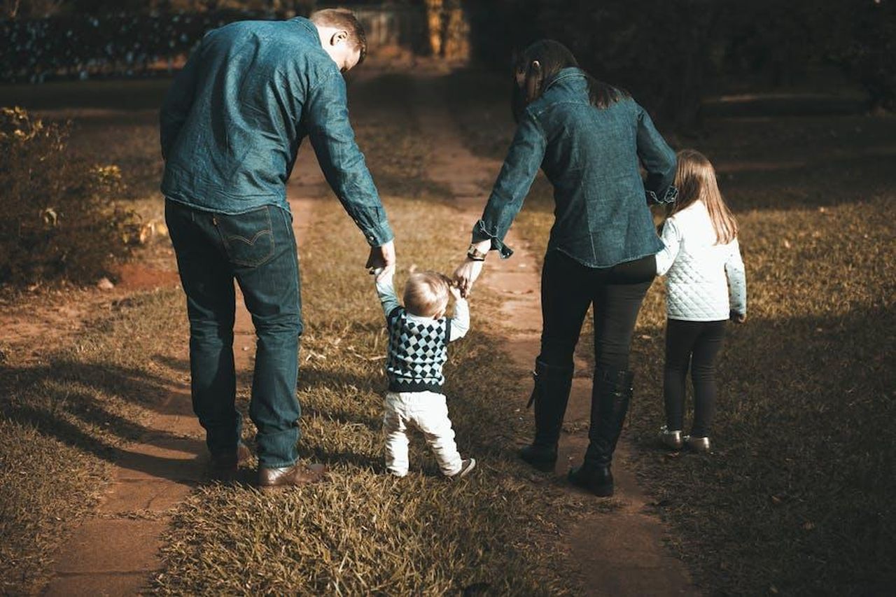 La_storia_della_loro_famiglia_e_dei_figli_cAO6oORSgK - Confidenze24 Source: Vidal Balielo Jr. - pexels - A family of four walks hand in hand on a path, enjoying a sunny day outdoors.
