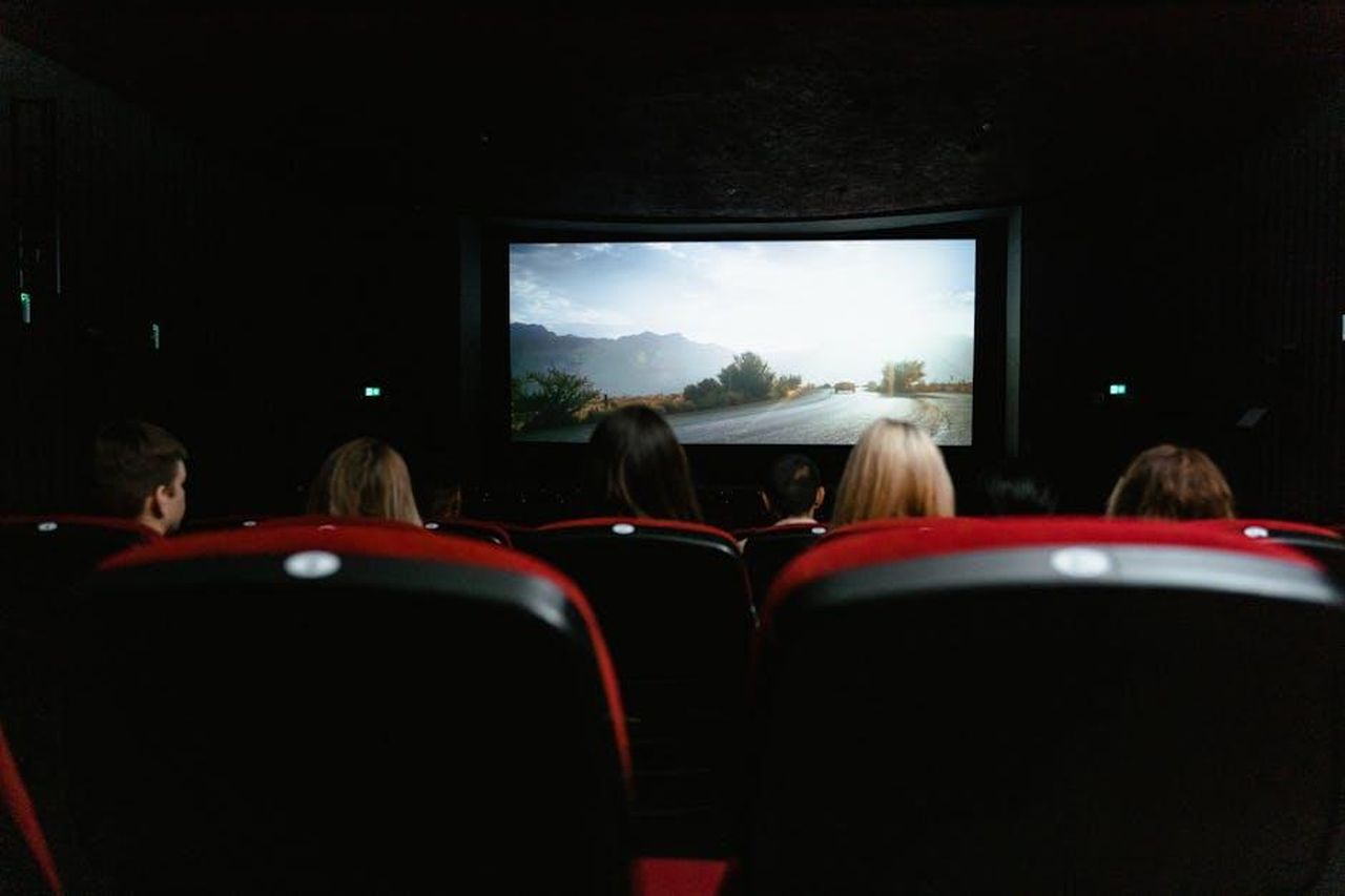 La_transizione_da_teatro_a_televisione_n6GNhVeB8v - Confidenze24 Source: Tima Miroshnichenko - pexels - View from behind of people watching a movie in a cinema with red seats and a large screen.