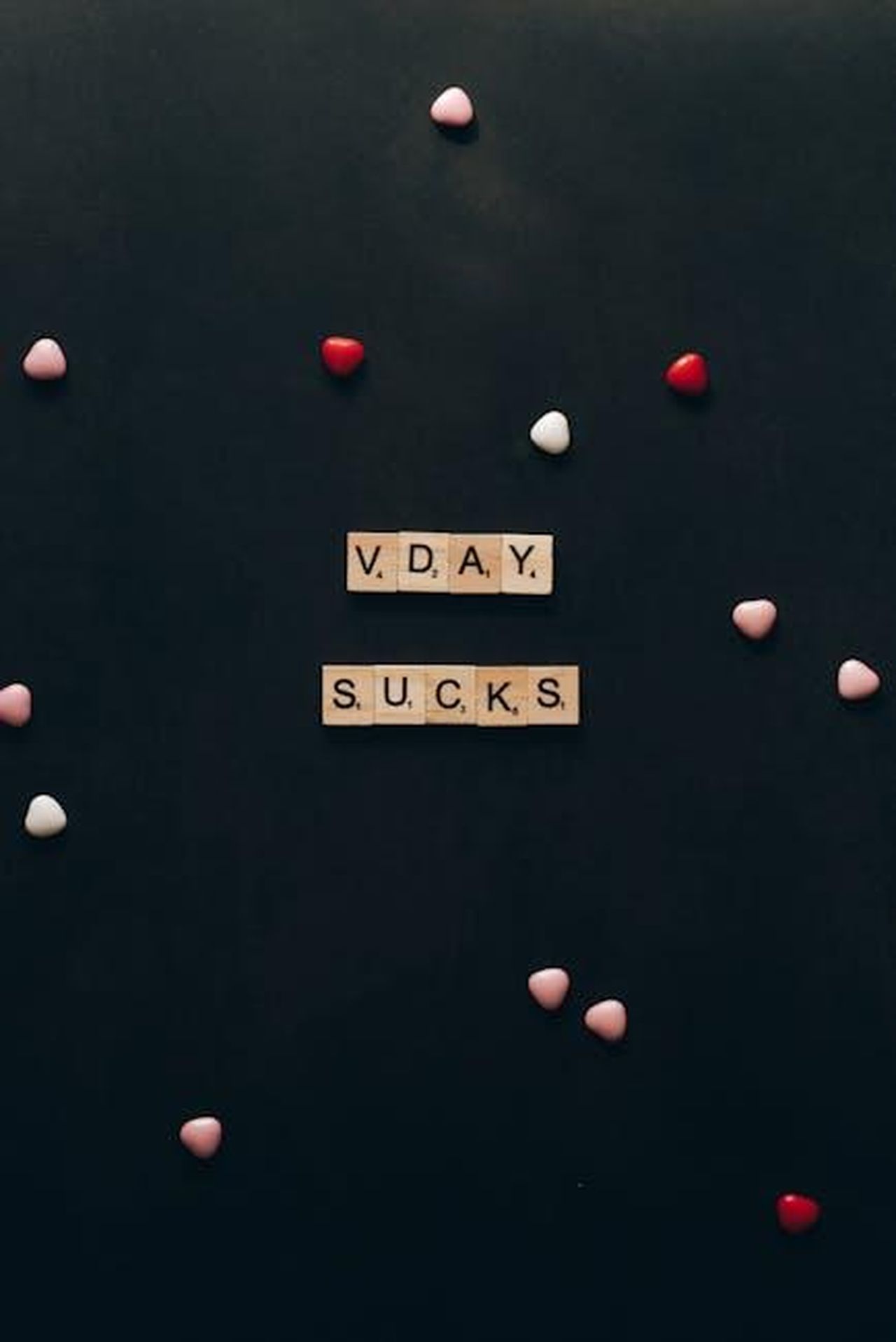 La_vita_da_single_di_Jennifer_Lopez_ezrTC81Bwg - Confidenze24 Source: Leeloo The First - pexels - Scrabble tiles spell out 'V DAY SUCKS' on a dark background with scattered heart-shaped decorations.