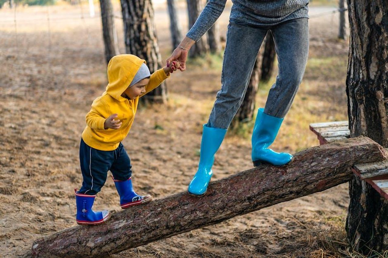 La_vita_familiare_dopo_gli_Oscar_fGXc8xkDOb - Confidenze24 Source: Alex P - pexels - A woman helps her toddler walk on a log in a park, showcasing child support and family bonding.