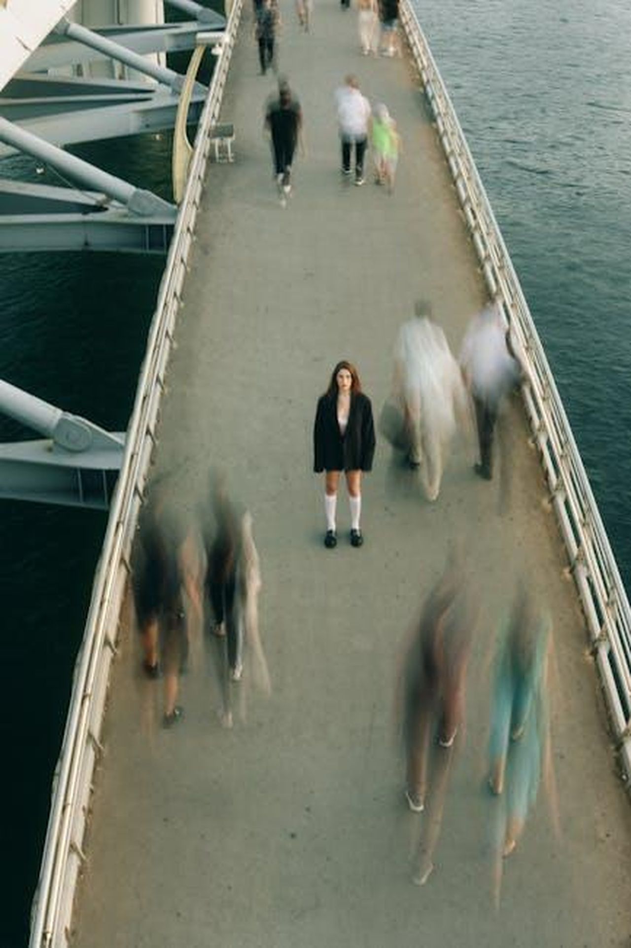 La_vita_quotidiana_di_Harry_6mvsBWDXEa - Confidenze24 Source: Göksu Taymaz - pexels - A woman stands still on a bustling footbridge, capturing a moment of solitude amidst motion.