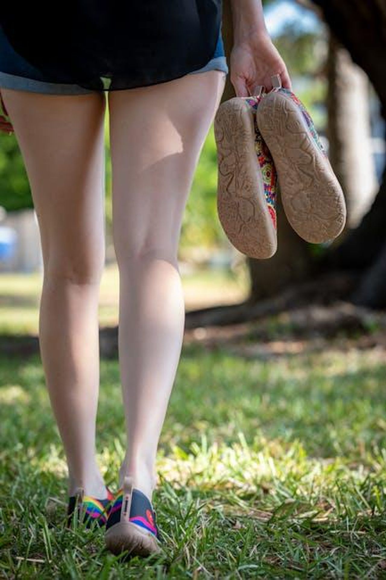 Lancio_della_collezione_Sperry_x_Aritzia_y3BTSpRToU - Confidenze24 Source: Connor McManus - pexels - A woman carries shoes while walking barefoot on grass in a sunny park.