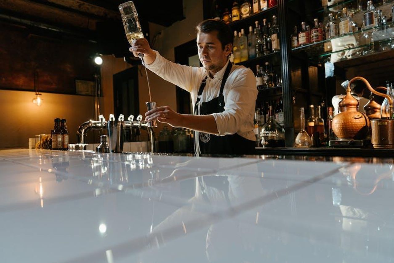 Lavoro_come_coat_check_in_un_bar_di_Chicago_VYHbSo6dB9 - Confidenze24 Source: cottonbro studio - pexels - A bartender expertly pours a drink at a modern bar with a variety of bottles in the background.