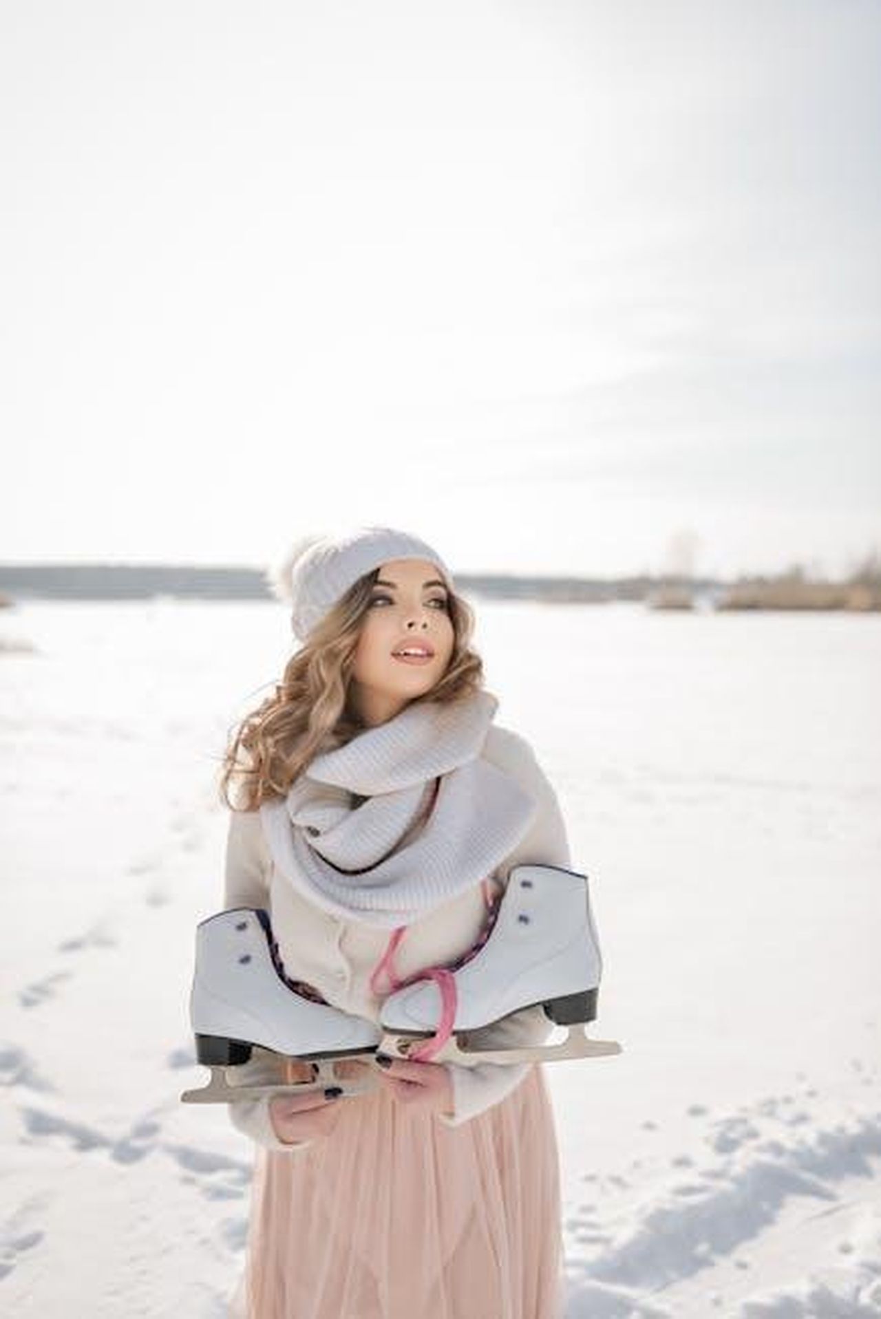Le_Aspettative_per_la_Stagione_8_di_Outlander_vPlEVfyFXd - Confidenze24 Source: Аня Кринцер - pexels - Smiling woman in winter attire holding ice skates on a sunny snowy day outdoors.