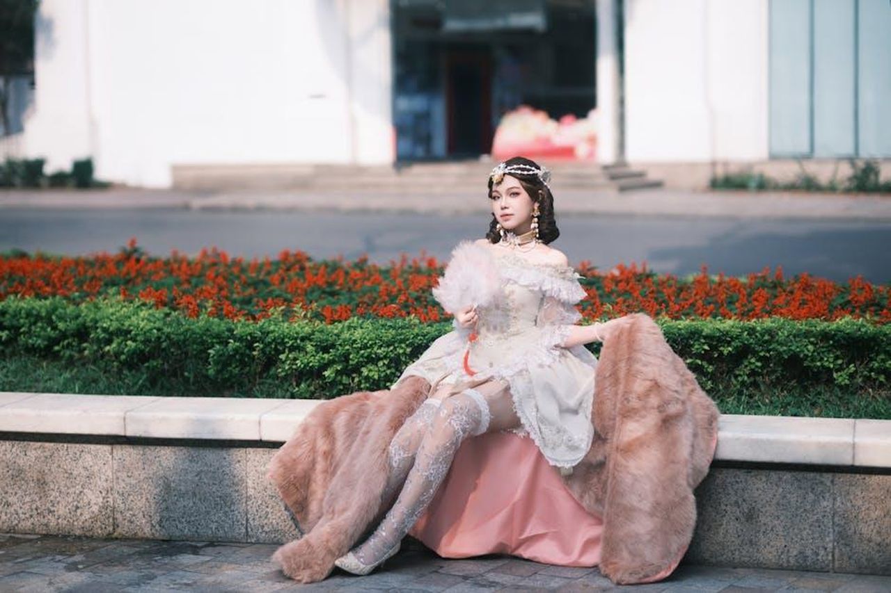 Le_Speculazioni_dei_Fan_ujBvrOeQK6 - Confidenze24 Source: TBD Tuyên - pexels - A woman dressed in a vintage Victorian costume sits gracefully outdoors, holding a delicate fan.