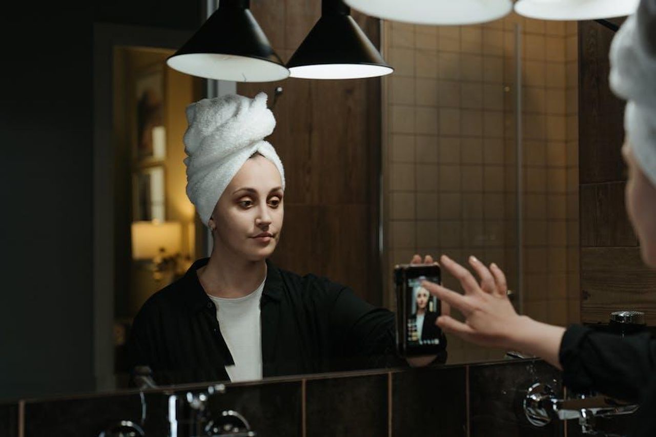 Le_Ultime_Accuse_di_Cardi_B_su_Instagram_Live_2DMgvsQVcL - Confidenze24 Source: cottonbro studio - pexels - A woman with a towel on her head takes a selfie in a stylish bathroom mirror.